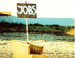 En lenestol står på en grusplass. Et håndlaget skilt med teksten "jobs" står opp fra stolen.