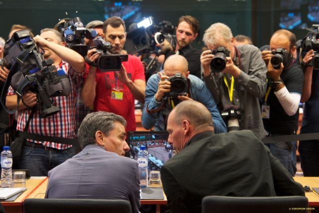 To menn snakker sammen ved et bord. Foran dem er en stor gruppe pressefotografer som tar bilder av dem.