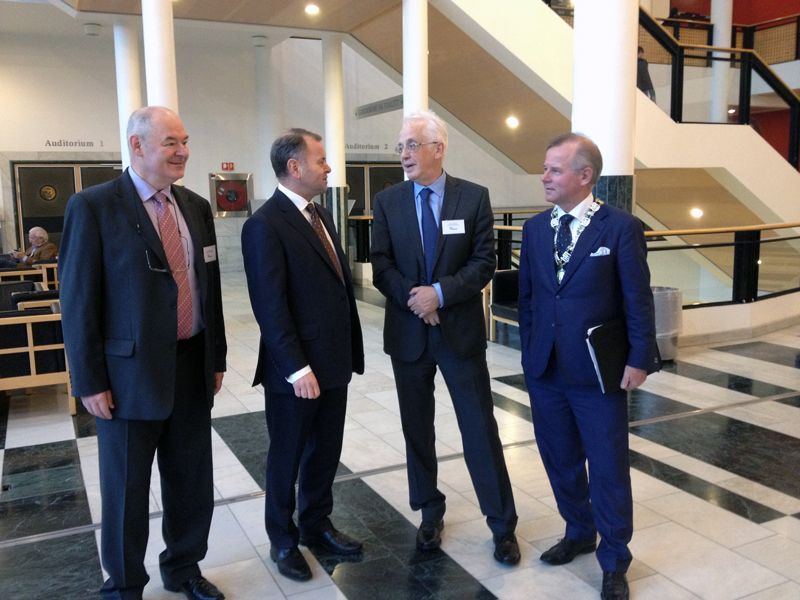Four men in suits (John Erik Fossum, Olemic Thommessen, Erik O. Eriksen and Ole Petter Ottersen) standing in a large aula.