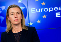 A woman (Federica Mogherini) in front of a blue screen with the European Union flag.