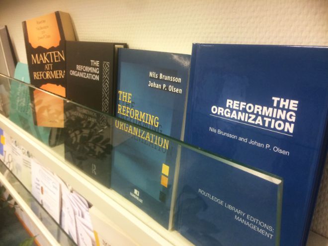 The four editions of the book 'the Reforming ORganization' by Johan P. Olsen standing in a row in a book shelf.
