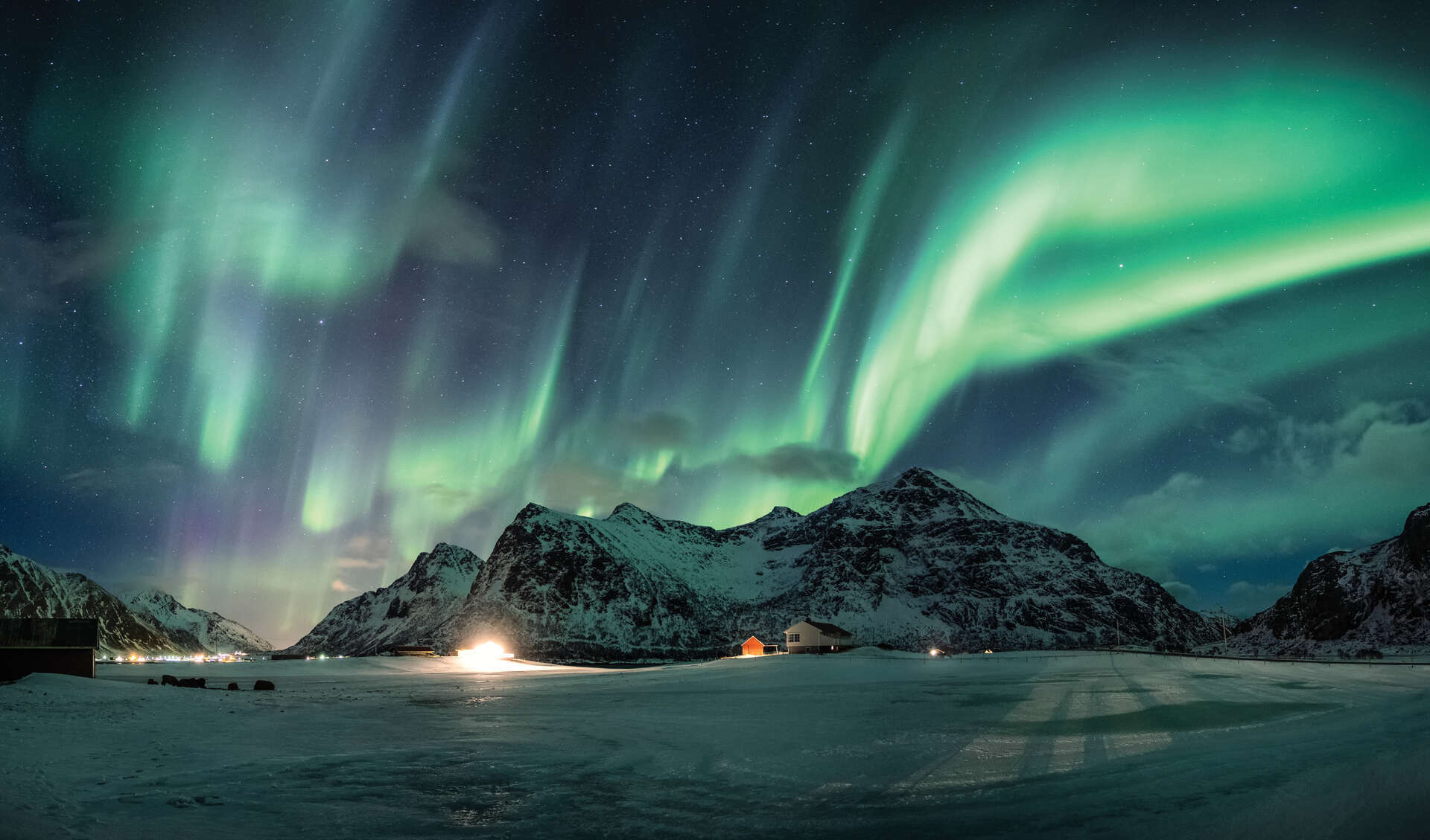 Aurora borealis eller nordlys over snøfjell på kystlinjen