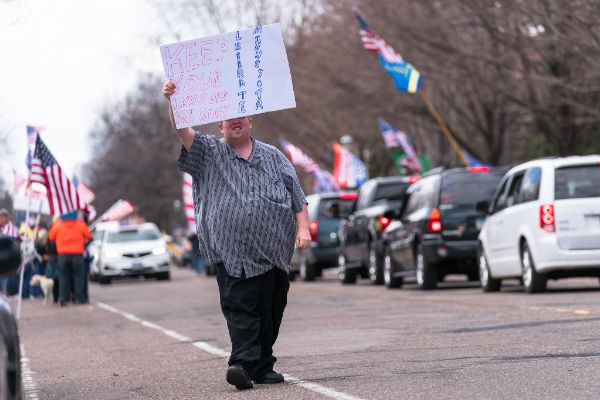 man walking on a road carrying a sign
