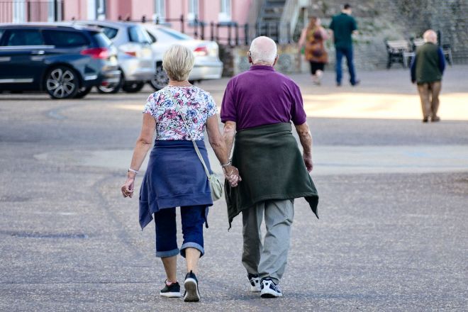 Eldre par som holder hender, fotografert bakfra