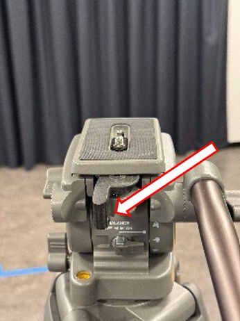 Quick-release plate on top of the tripod, with an arrow showing the black lever to pull to release it