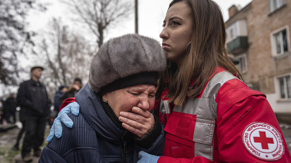 En gråtende kvinne får trøst av en hjelpearbeid fra Røde kors