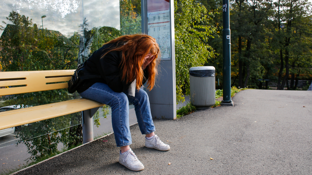 deprimert jente på et busstopp med ansiktet gjemt i hendene
