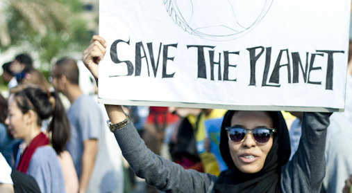 En kvinne i folkemendge holder en plakat hvor det står Save the planet