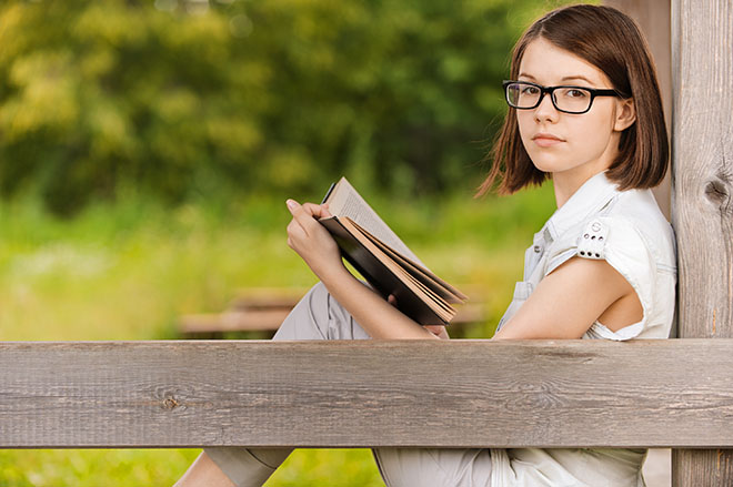 Tenåringsjente med brikker som sitter på benk og leser