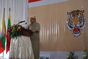 Mann på talerstol med tigersymbol på veggen