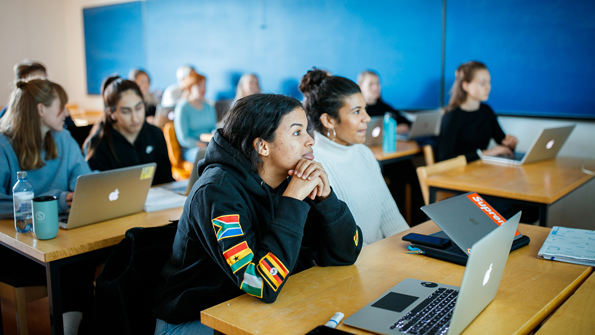 Studenter i et seminarrom med laptoper framfor seg fokuserer på foreleser