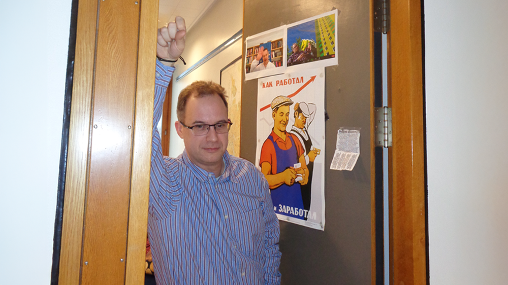 Mann med briller foran kontordør med plakater 
