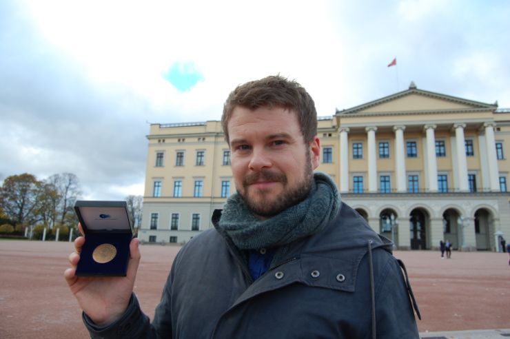 en mann står foran slottet og holder opp en medalje