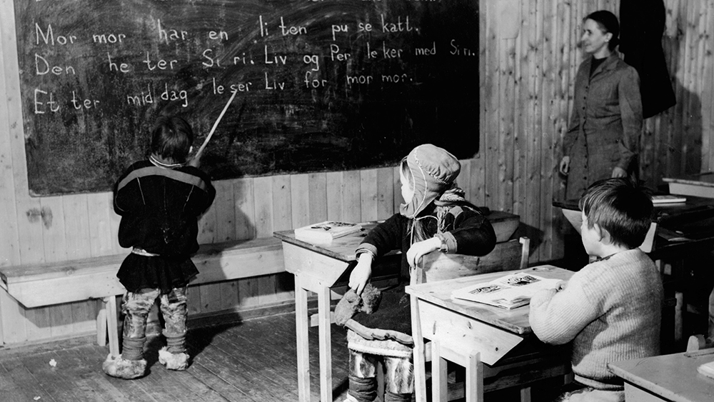 Samisk gutt ved skoletavle med norske setninger.