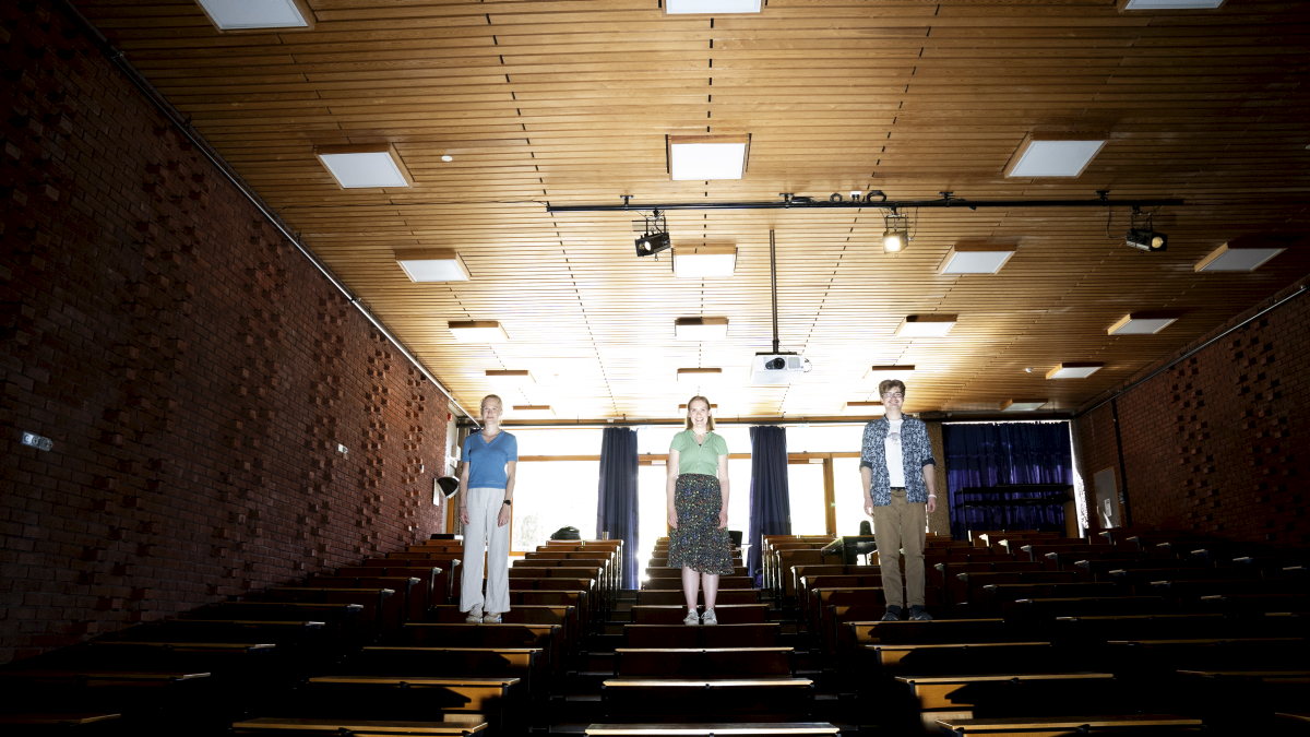 Three students standing on tables in an auditorium.
