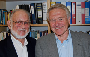 Two smiling men in front of a book shelf.