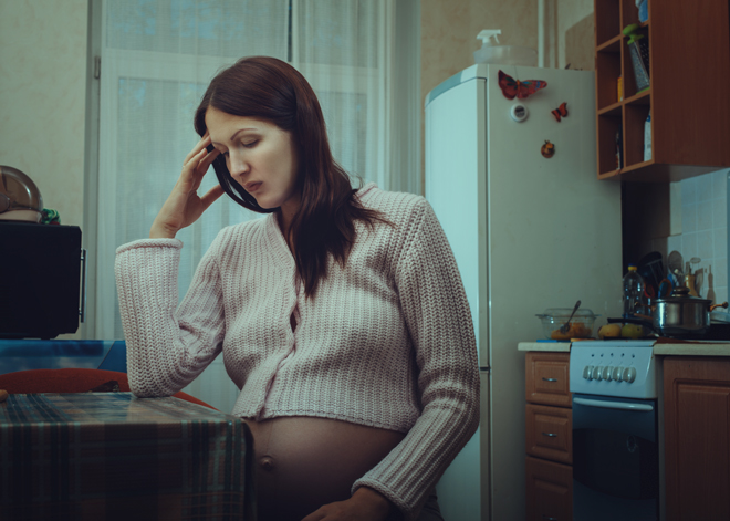 Gravid, trist kvinne sitter ved et bord.
