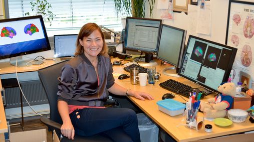 En smilende kvinne (professor Kristine Walhovd) sitter ved en kontorpult med flere skjermer.