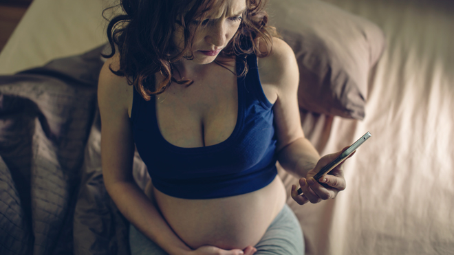 Gravid kvinne har vondt i magen og ser på mobilen