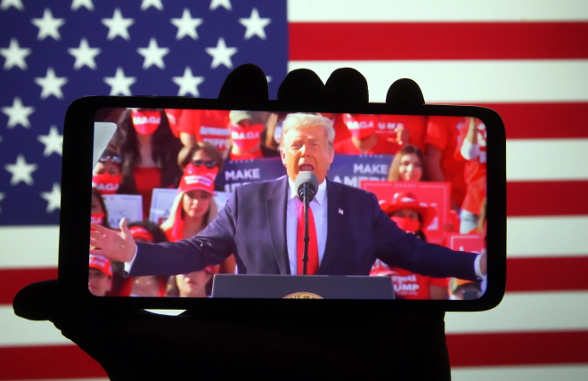 En hånd holder en mobil med en video av Donald Trump foran et amerikansk flagg.
