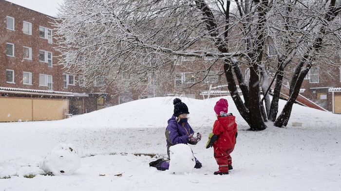 To barn om leker i snøen og lager snømann mellom noen blokker 