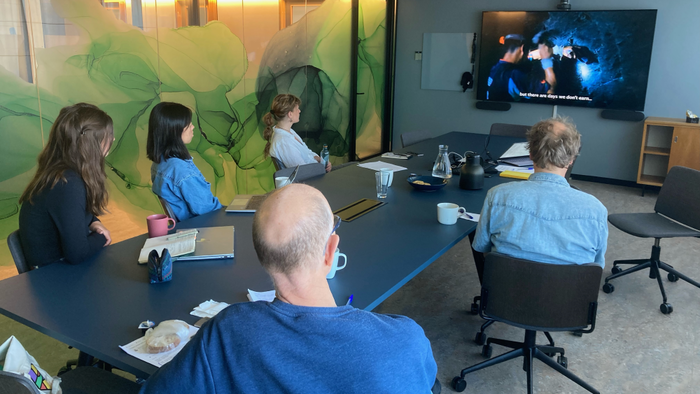Five people in a meeting room looking at a TV screen