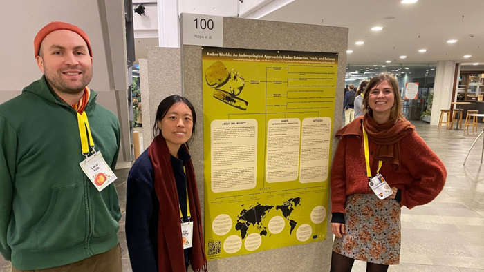 Three members of the amber team standing next to a poster