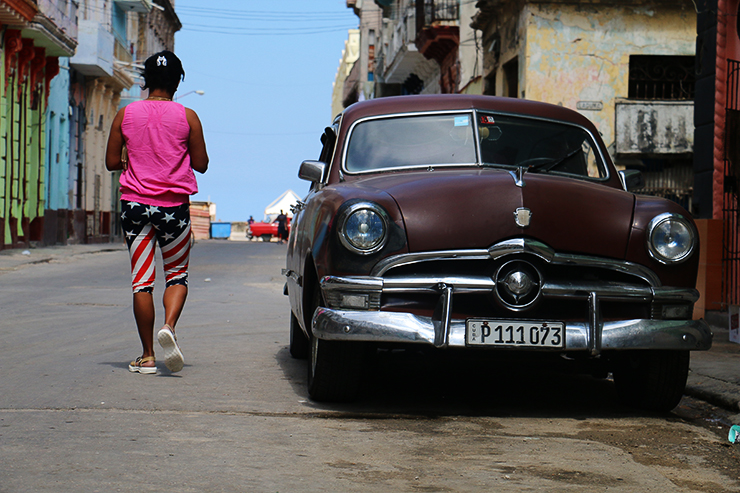 Kubansk kvinne med amerikatights passerer gammel bil på gata