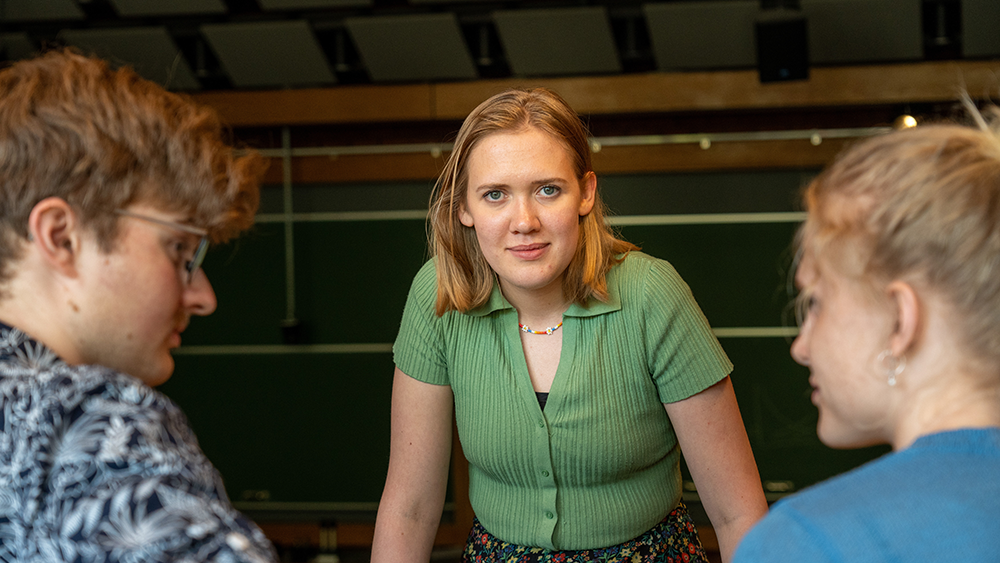 Three students in a lecture hall, girl in the middle making eye contact