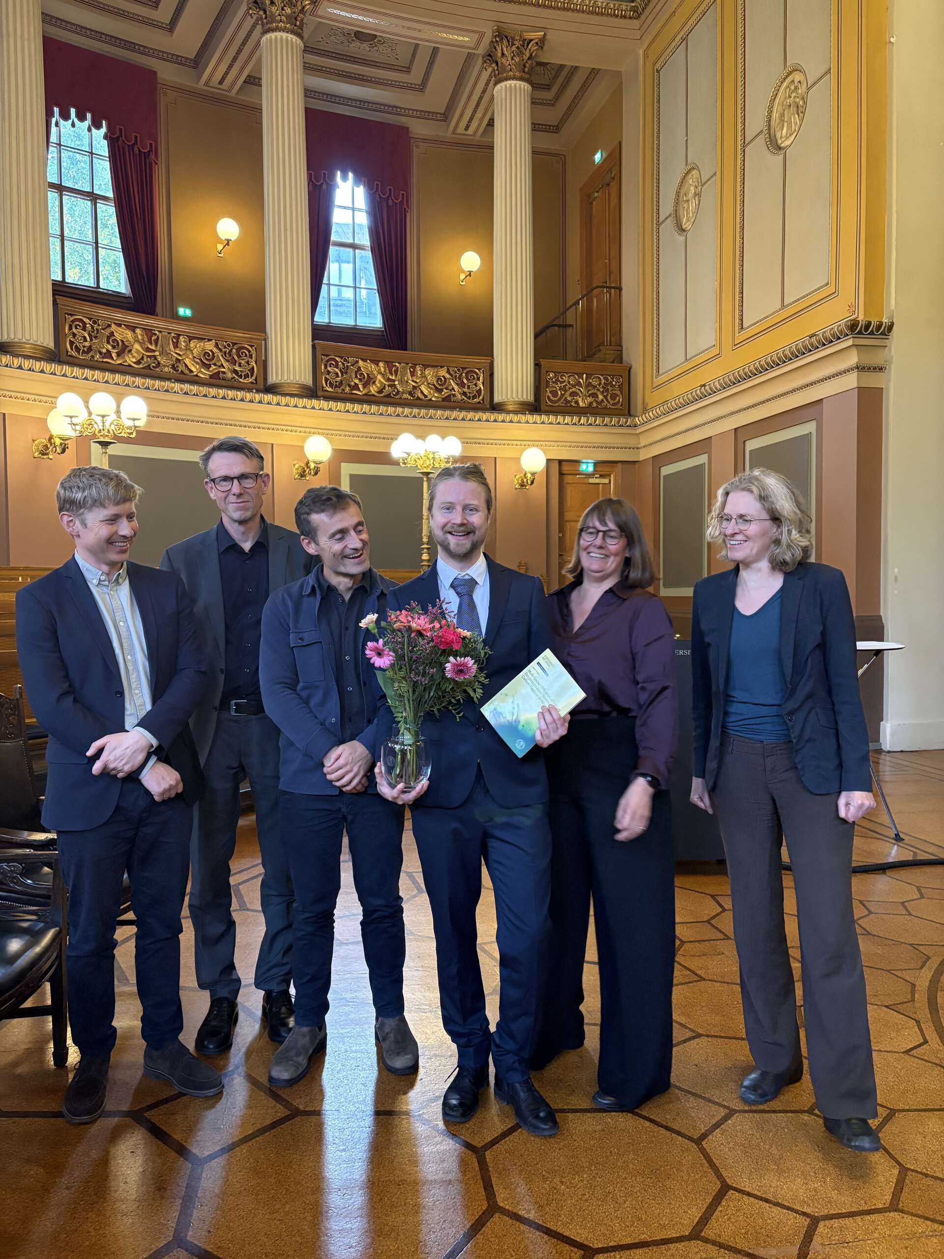 Bildet kan inneholde: formelt antrekk, stående, interiørdesign, frakk, dress.