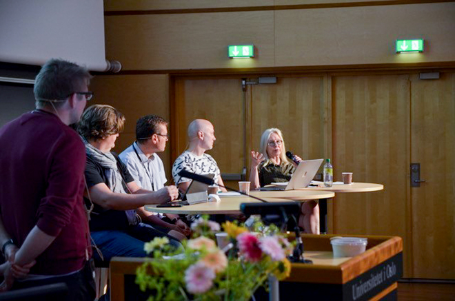 Fire personer i panelsamtale i et auditorium.