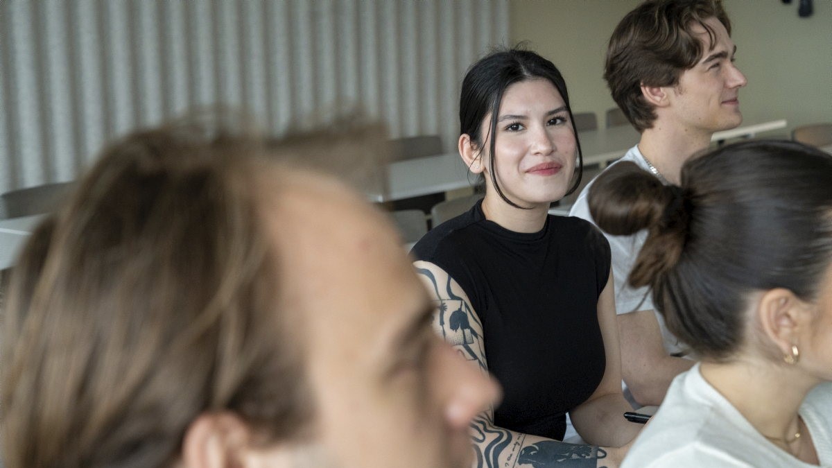 Studenter i et klasserom. Én av dem ser rett i kamera.